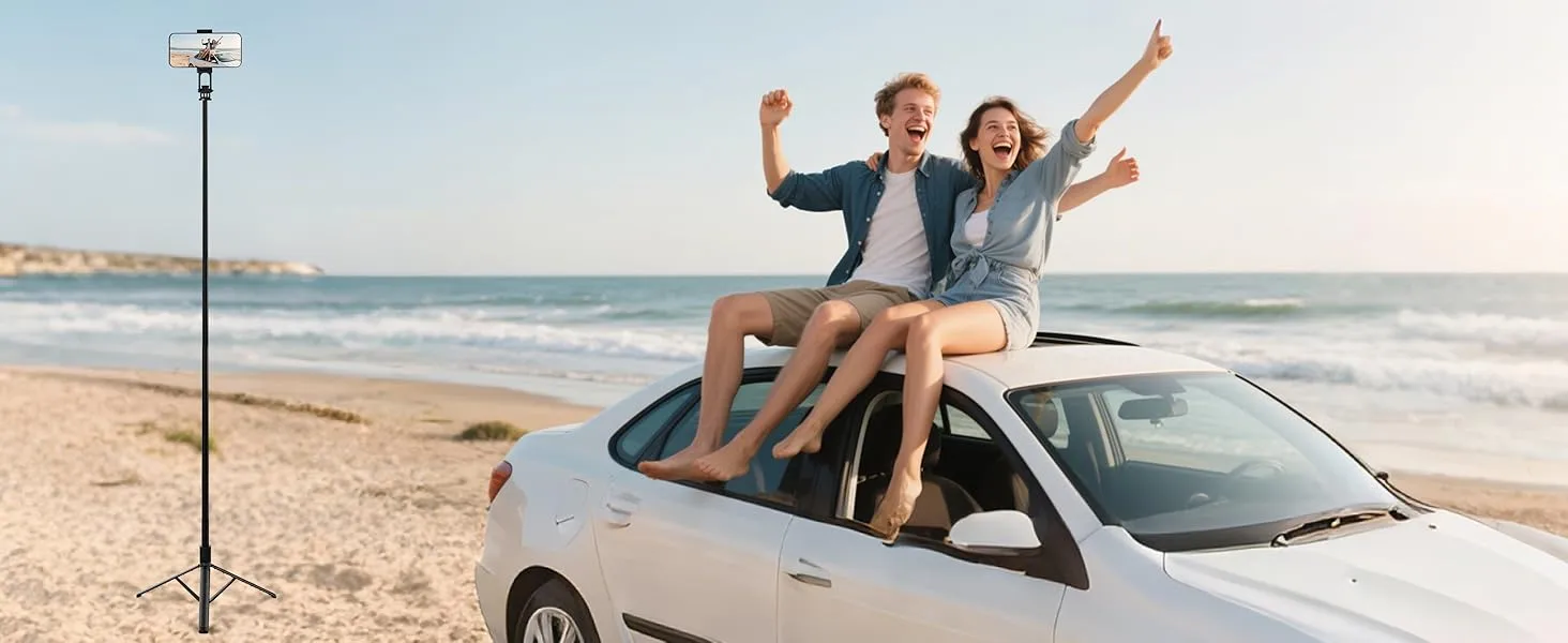 Two people sitting on top of a white car parked on a beach, raising their arms in celebration. A camera tripod stands in the foreground.