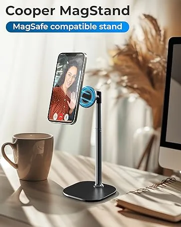 Cooper MagStand phone holder with MagSafe compatibility, featuring adjustable height black metal stand on desk with coffee cup nearby.